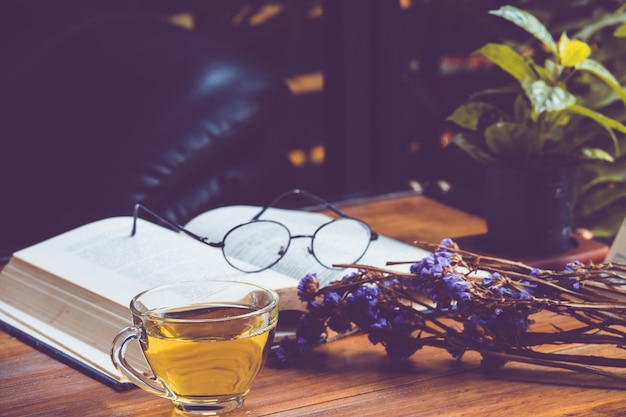 Hot tea in a cup with old book and flower on table