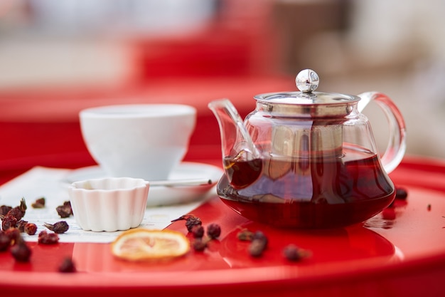 Hot tea in glass teapot and cup, on red background