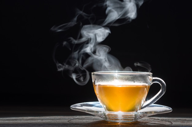 Foto tè caldo in teiera e tazza di vetro con vapore su fondo di legno