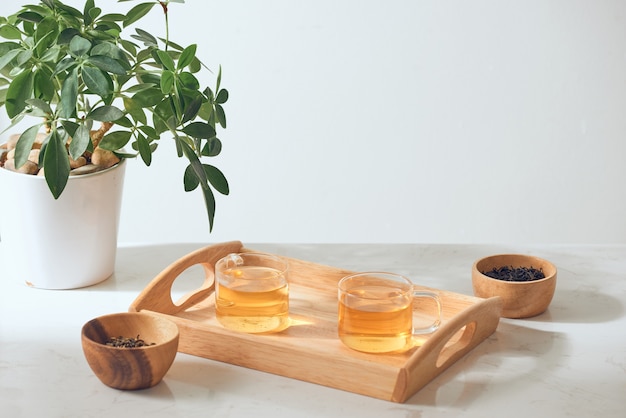 Hot tea is in the glass. Placed on a wooden tray.