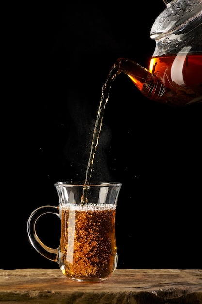 Hot tea pours into a transparent mug on a black background