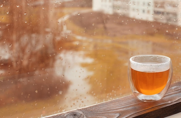Горячий чай в термостекле на фоне осеннего окна с каплями дождя