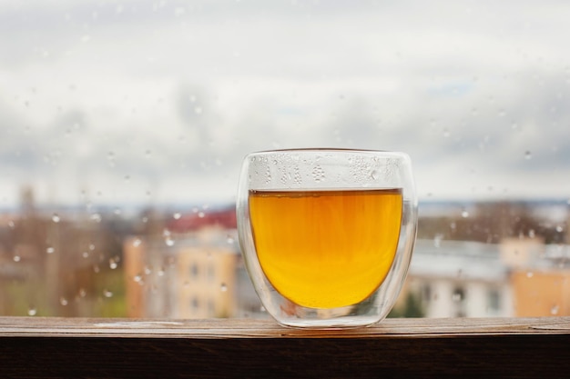 Горячий чай в термостекле на фоне окна с каплями дождя