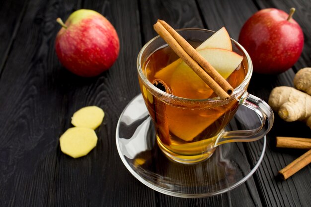 Photo hot tea with apples, cinnamon and ginger in the glass cup on the black