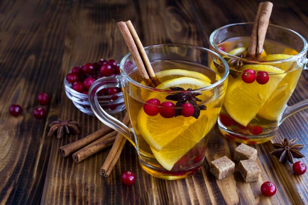 Hot tea with lemon, cinnamon, cranberry and anise in the glass cups on the wooden background. Close-up. Winter drink.