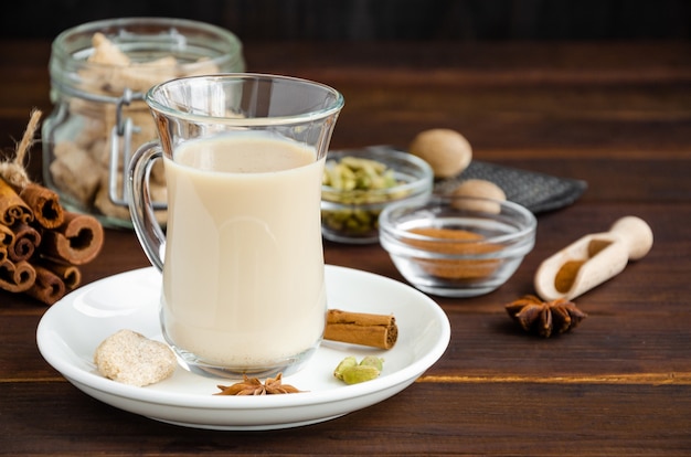 Hot tea with milk, cinnamon, cardamom, anise and other spices, Indian masala tea in a glass cup on a wooden background. copy space.