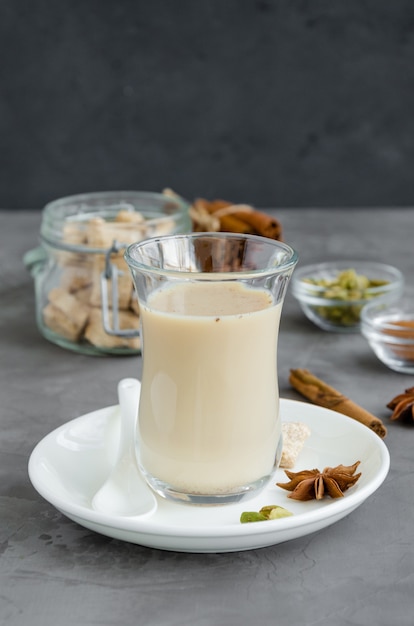 Hot tea with milk, cinnamon, cardamom, anise and other spices, Indian masala tea in a glass on a dark background. Vertical, copy space.