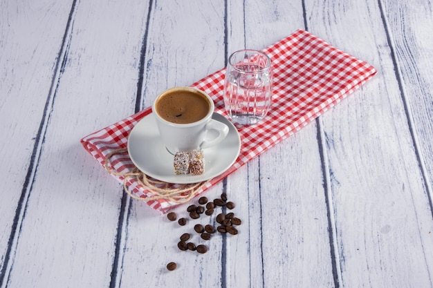 Foto caffè turco caldo in tazza bianca con delizia e fagioli su fondo di legno bianco su panno rosso