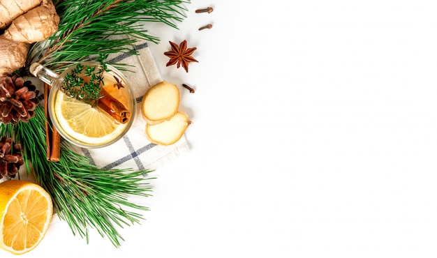 Hot winter aromatic drink. Ginger tea with lemon, cinnamon, star anise, cones and green Christmas tree branches on a white background, top view, flat lay, copy space.