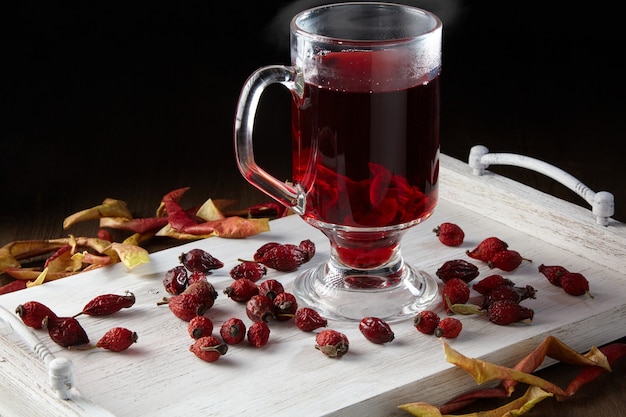 Hot winter drink surrounded by dried rose hips and apples on a white painted wooden tray