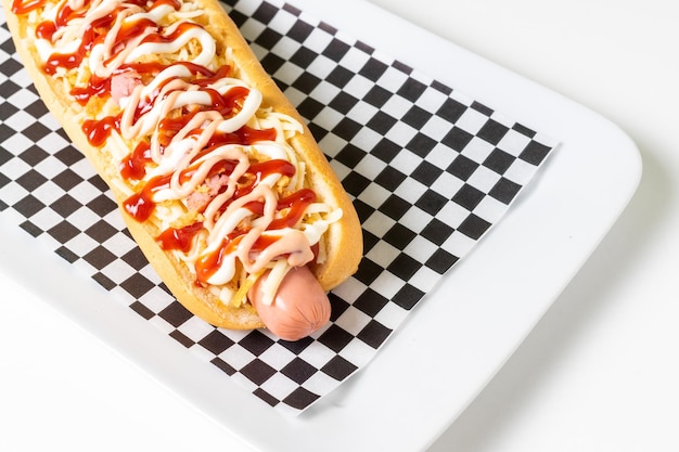 Hotdog met diverse sauzen, patat en kaas op een zwart wit geruit servet.