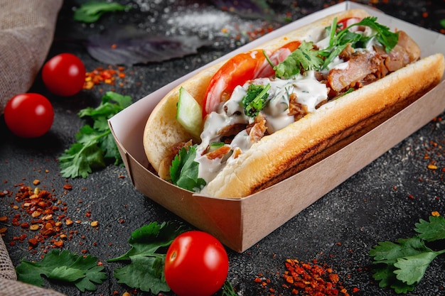 Hotdog met groenten gevuld met kippenrundvlees en kruiden op een donkere stenen tafel Het concept van fastfood- en bezorgrestaurants