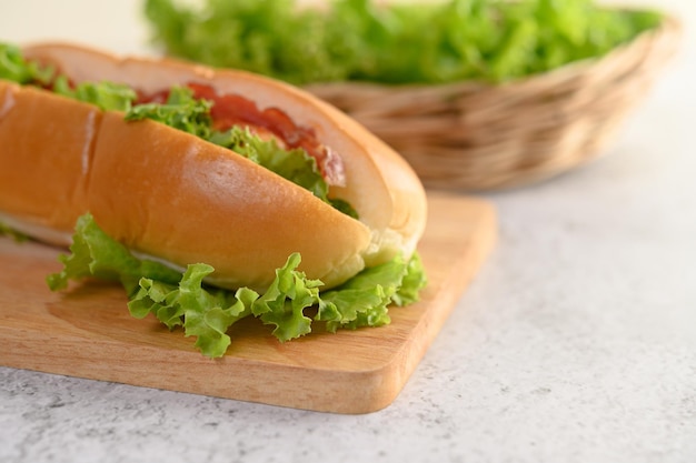 Hotdog on wood cutting board and blurred background with lettuce in weave basket copy space