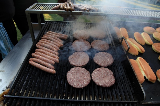 Hotdogs en hamburgervlees worden gekookt op een zwarte grill bovenop rook bij een openluchthamburger