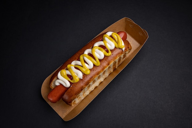 Hotdogs in papieren borden met worstjes en saus op een zwarte achtergrond