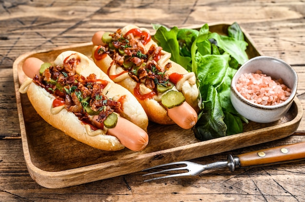 Hotdogs met gebakken spek, ui en ingelegde komkommers.