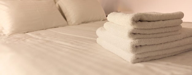 Hotel bedroom White fluffy folded towels linen sheets and pillows on bed Close up view