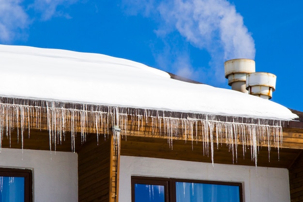 Hotel exterior in ski resort, snow, sunny day and ice. Windows and roof.