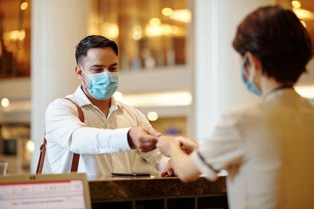 Receptionist dell'hotel che fornisce la chiave digitale della camera all'ospite in maschera medica