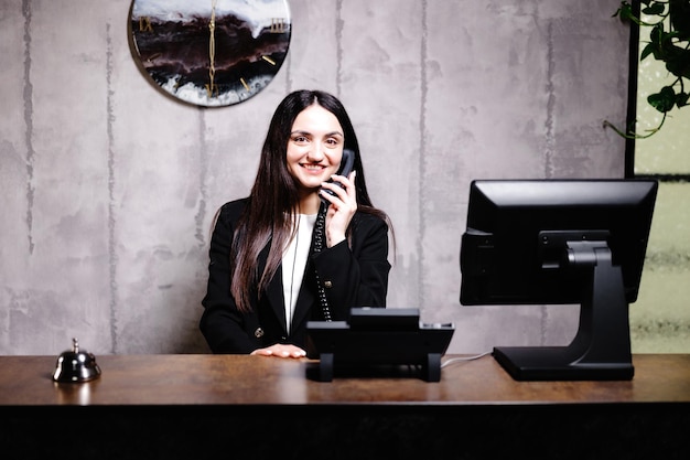 Photo hotel receptionist modern hotel reception desk with bell happy female receptionist worker standing at hotel counter and talking to phone