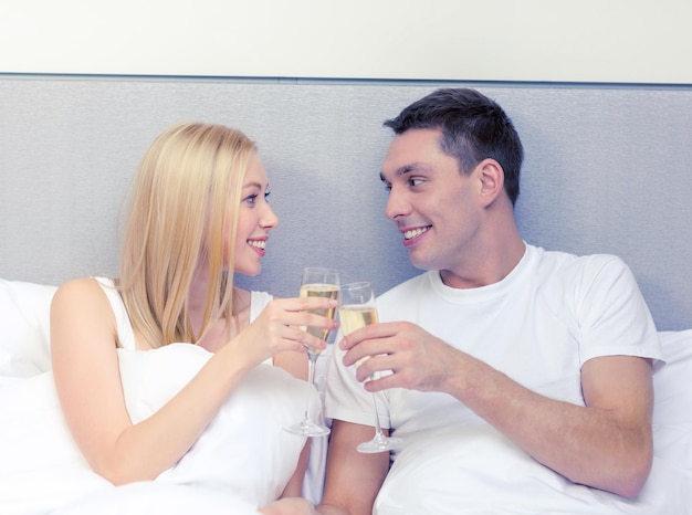 hotel, reizen, relaties en geluk concept - glimlachend paar met champagneglazen in bed