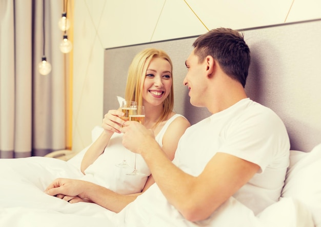 hotel, reizen, relaties en geluk concept - glimlachend paar met champagneglazen in bed