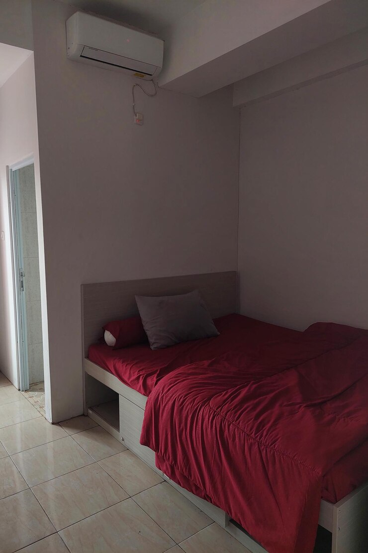 The hotel room is white with a red bed and sheets and an AC