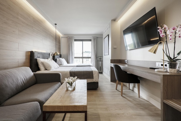 Photo hotel room with double beds sofa bed upholstered in leather wooden coffee table desk and large flat screen tv on the wall