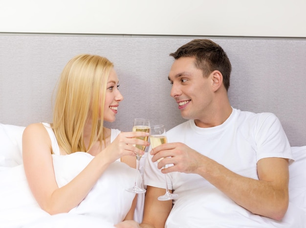 Concetto di hotel, viaggi, relazioni e felicità - coppia sorridente con bicchieri di champagne a letto Foto Premium