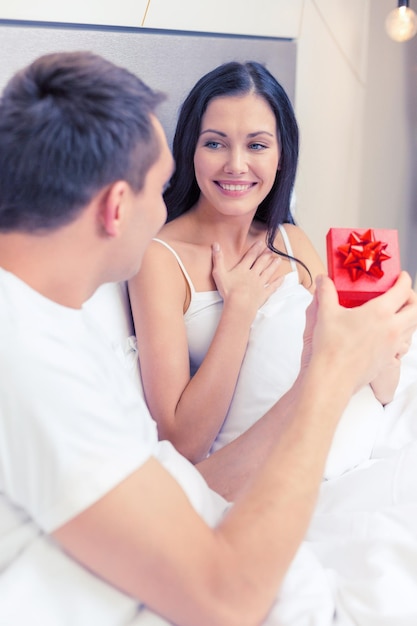 hotel, travel, relationships, holidays and happiness concept - man giving woman little red gift box