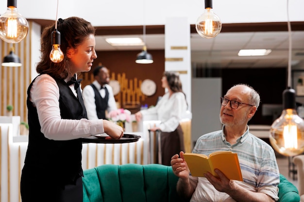 Фото Отельная официантка, обслуживающая пожилого человека.