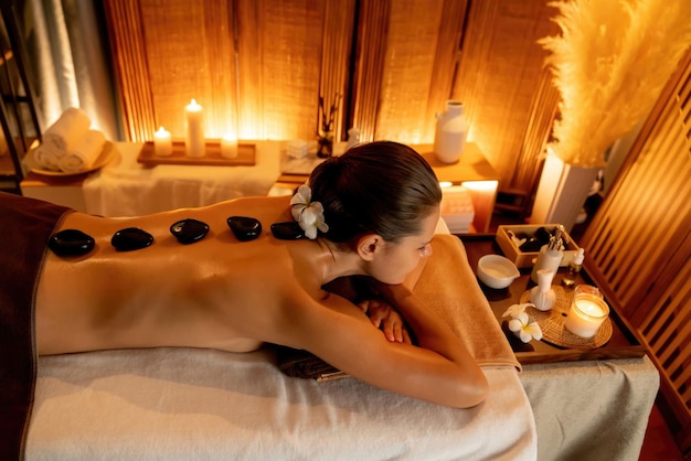 Hotstone-massage in spa salon in luxeresort met warm kaarslicht zalige vrouw klant genieten van spa basaltsteenmassage glijden over lichaam met rustgevende warmte Rustig