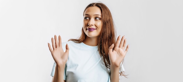 Hou op. de vrouw heft haar handen op naar de camera. het model voelt zich verward en weet niet wat te kiezen. mooie zoete brunette meisje met fashion make-up paarse lippen op een afgelegen grijze achtergrond