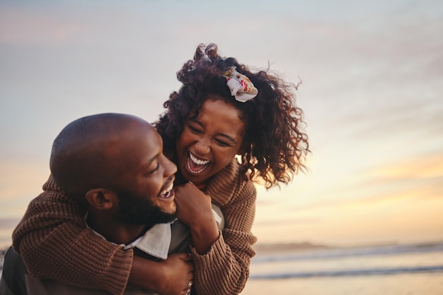 Hou van reizen en leuk koppel op het strand genieten van zomervakantie of huwelijksreis bij zonsondergang met een ritje op de rug terwijl ze speels zijn Lachende energie en vakantie aan zee met zwarte man en vrouw samen