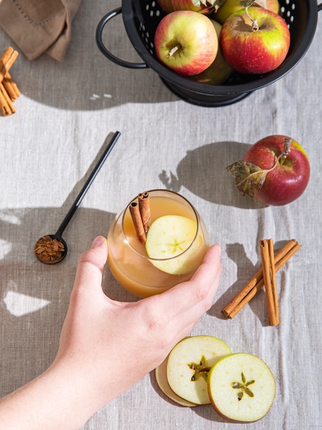 Houd een glas vers gezette appeldrank vast met appelschijfjes en kaneel op linnen tafelkleed. bovenaanzicht en plat leggen