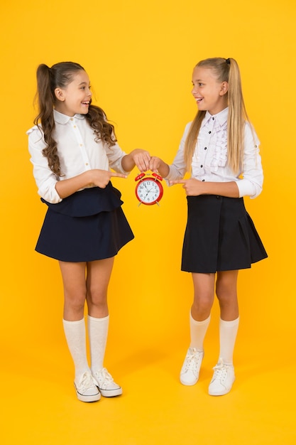 Houd uw studenten veilig en op tijd Gelukkige kleine meisjes die retro klok houden tijdens schooltijd op gele achtergrond Klein kind die wekker houden Tijd om te leren Schoolklok en tijdoplossing