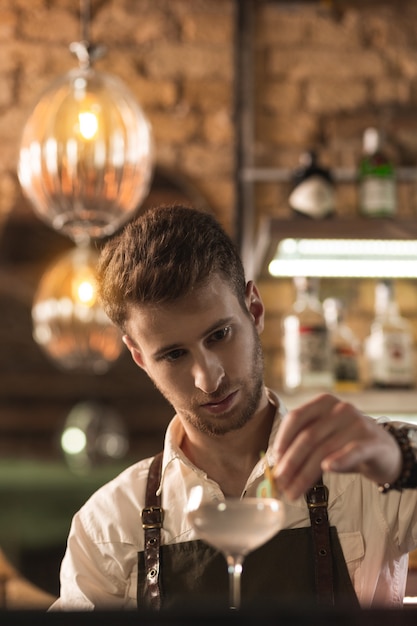 Houd van decoraties. Knappe jongeman die als barman werkt en een versiering op het glas zet terwijl hij zijn cocktail opsiert