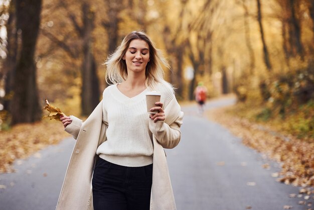 Houdt een kopje drank vast. Portret van een jonge brunette die overdag in het herfstbos is.