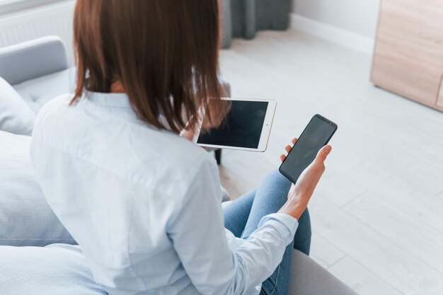 Houdt smartphone en tablet Jonge vrouw is overdag binnenshuis in de kamer van een modern huis