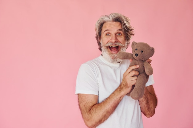 Houdt teddybeer vast Stijlvolle moderne senior man met grijs haar en baard is binnenshuis