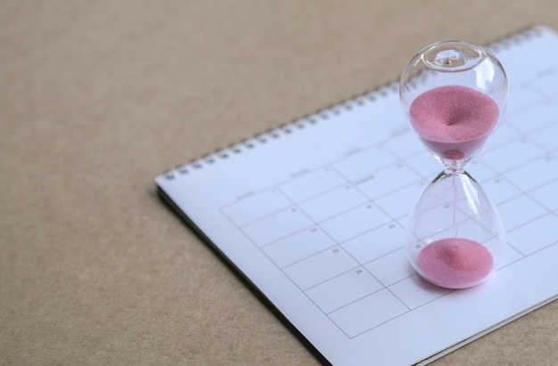 Hour glass with sand flowing on top of calendar