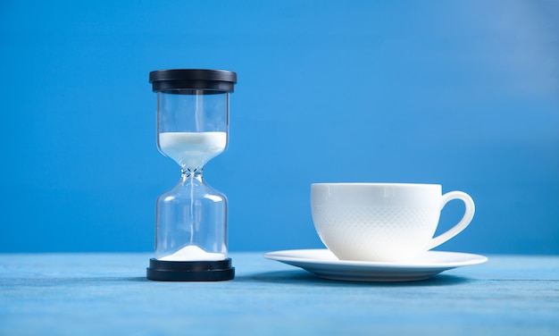 Hourglass and coffee cup on the blue background.