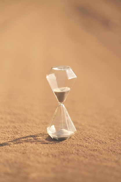 An hourglass on hot sand in desert in hot summer sun.