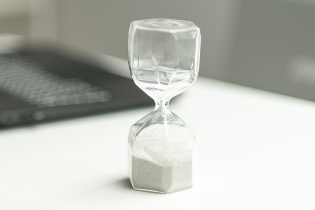 Hourglass near laptop computer concept for time management and countdown to deadline