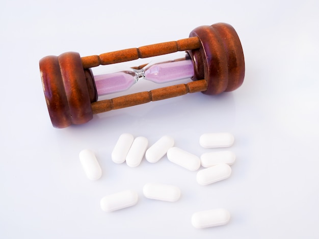 Hourglass and painkiller, medicine tablets, time and health care concept. Isolated on white surface.