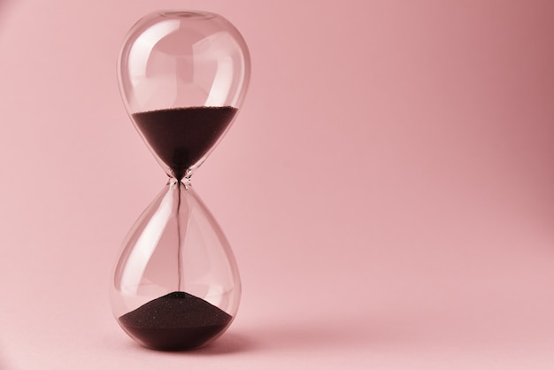 Photo hourglass on pink background, close up. urgency and running out of time concept