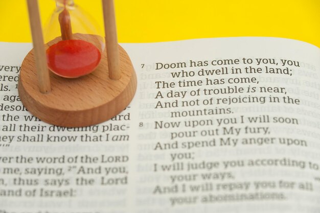 Photo hourglass on top of an open holy bible in the book of the ezekiel chapter 7 highlighted in verse 7