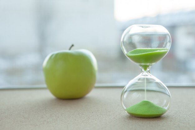 Hourglass with an apple in the background, close-up