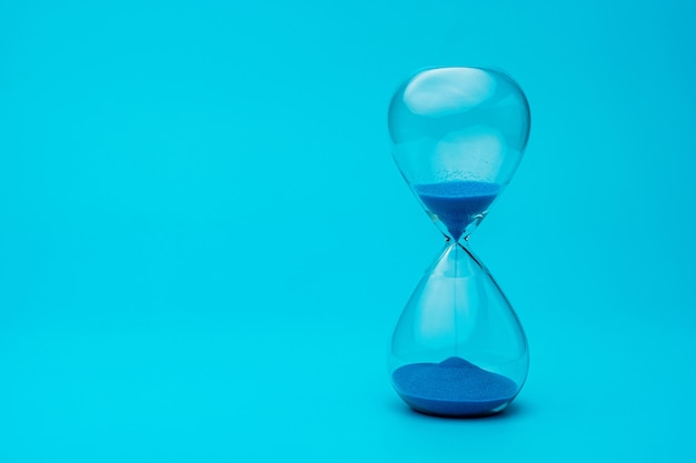 Hourglass with blue sand on blue background