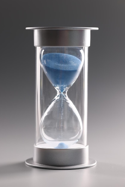 Hourglass with blue sand on gray background